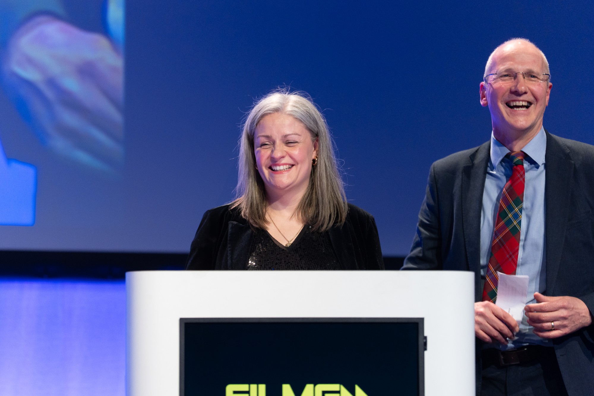 Two presenters laughing at the lectern at the Film G Awards