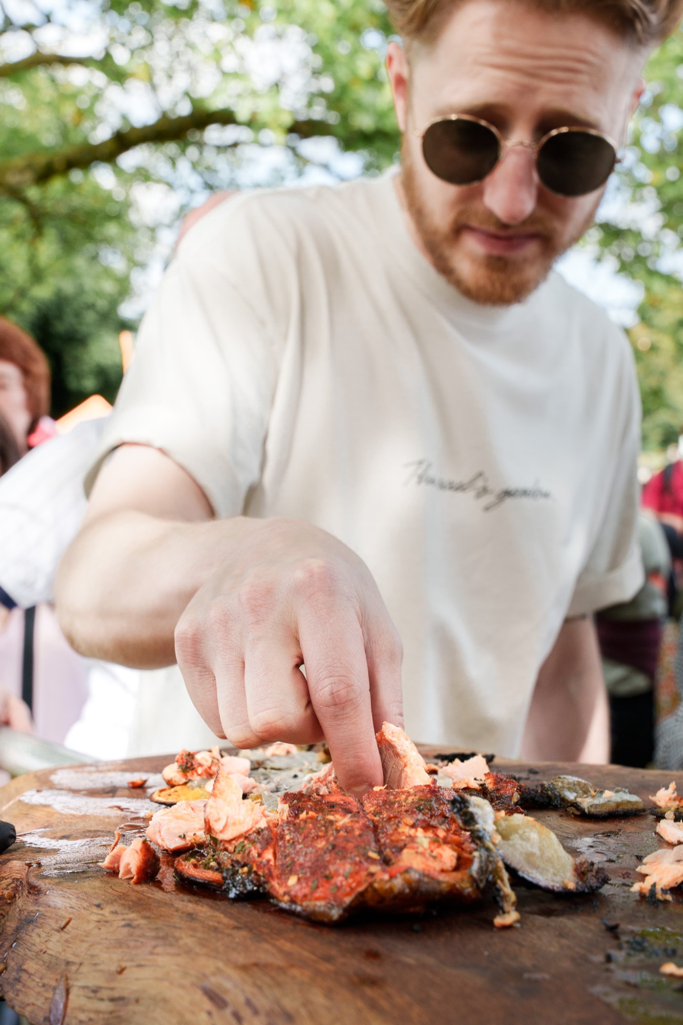 A man in sunglasses pulling apart fire-cooked salmon on a wooden board at Foodies Festival, Glasgow