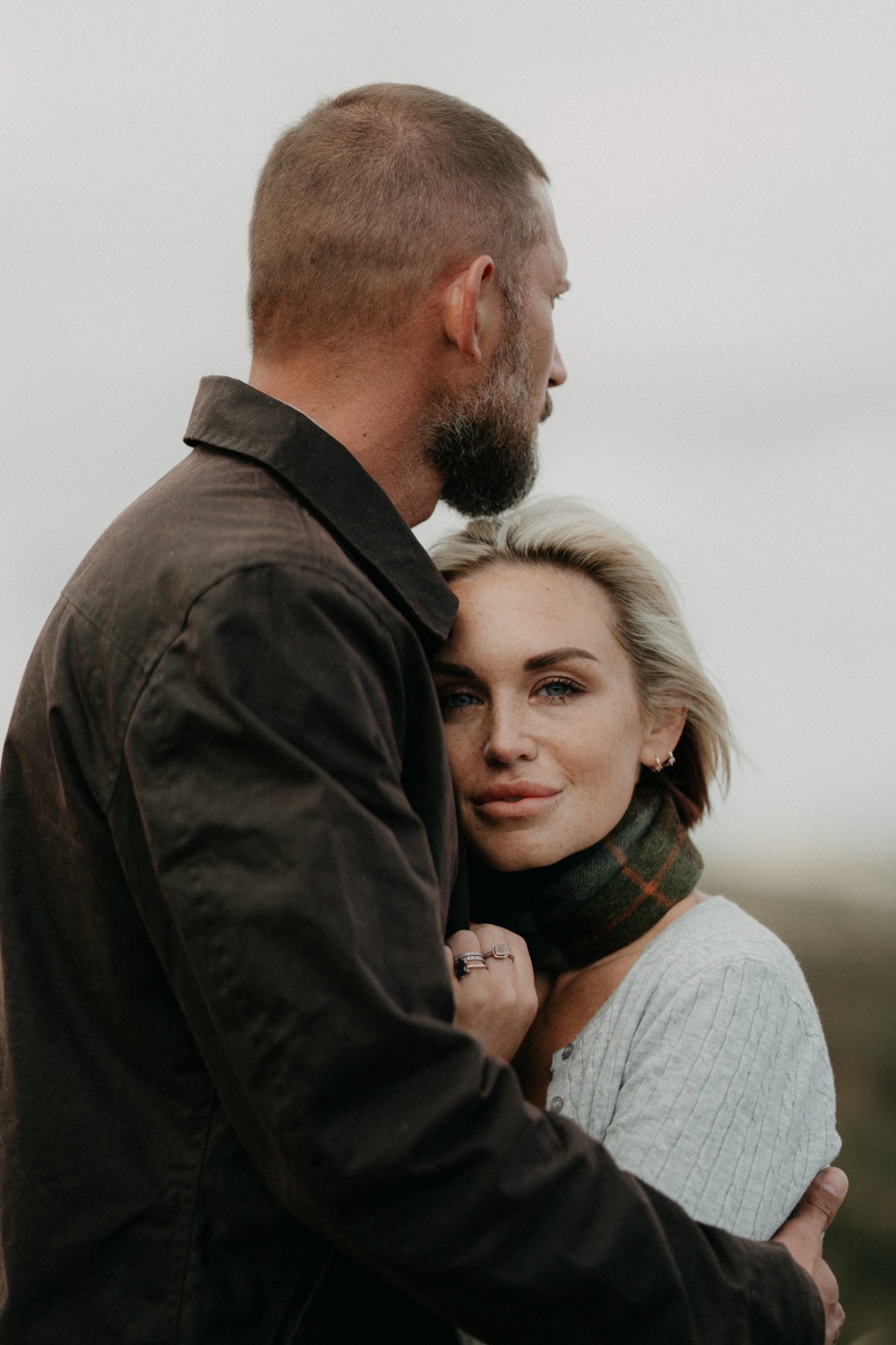 A man holding a woman close, her head against his chest as she looks at the camera
