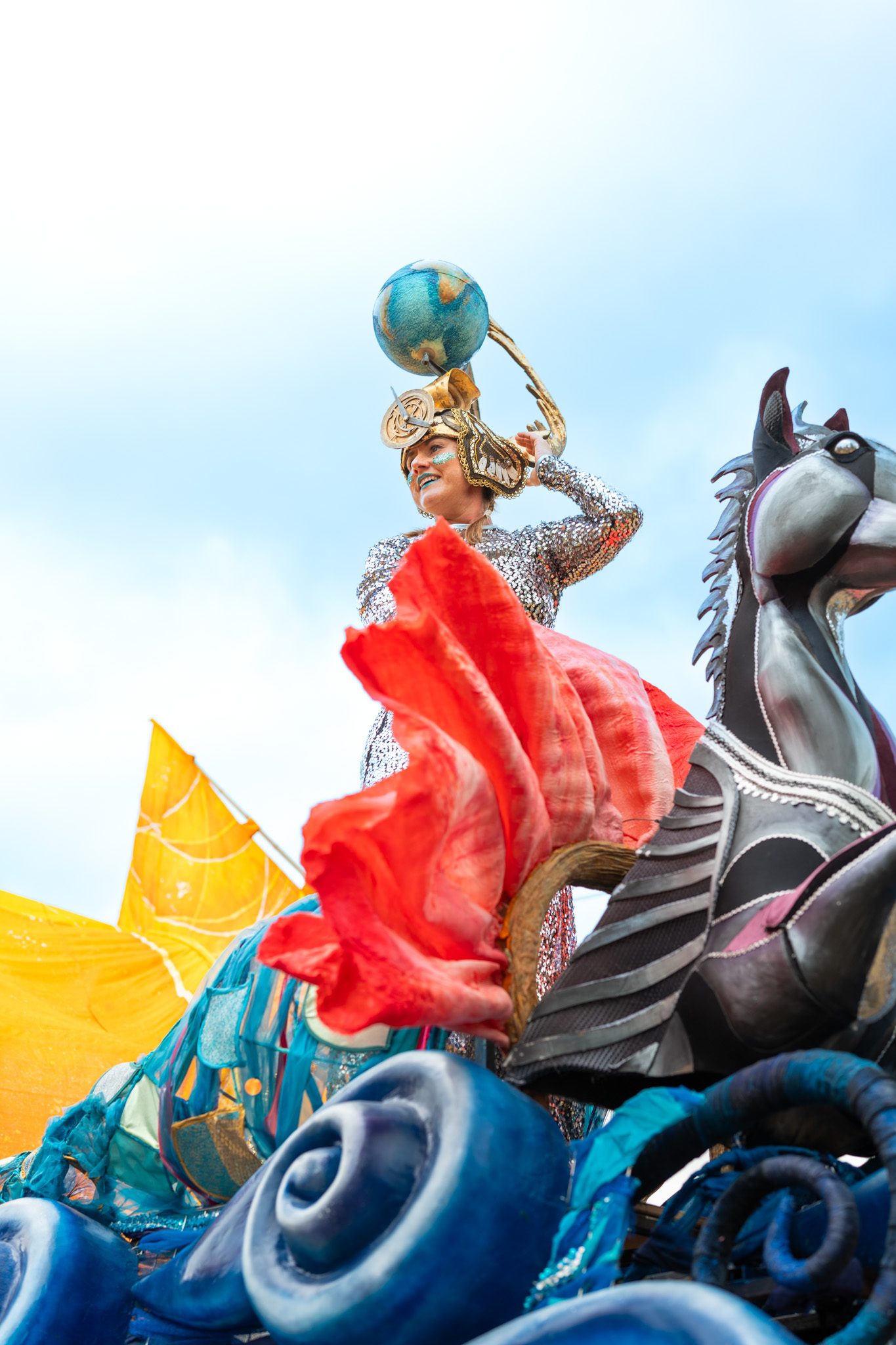 A performer on a parade float at Kendal Calling, against a blue sky
