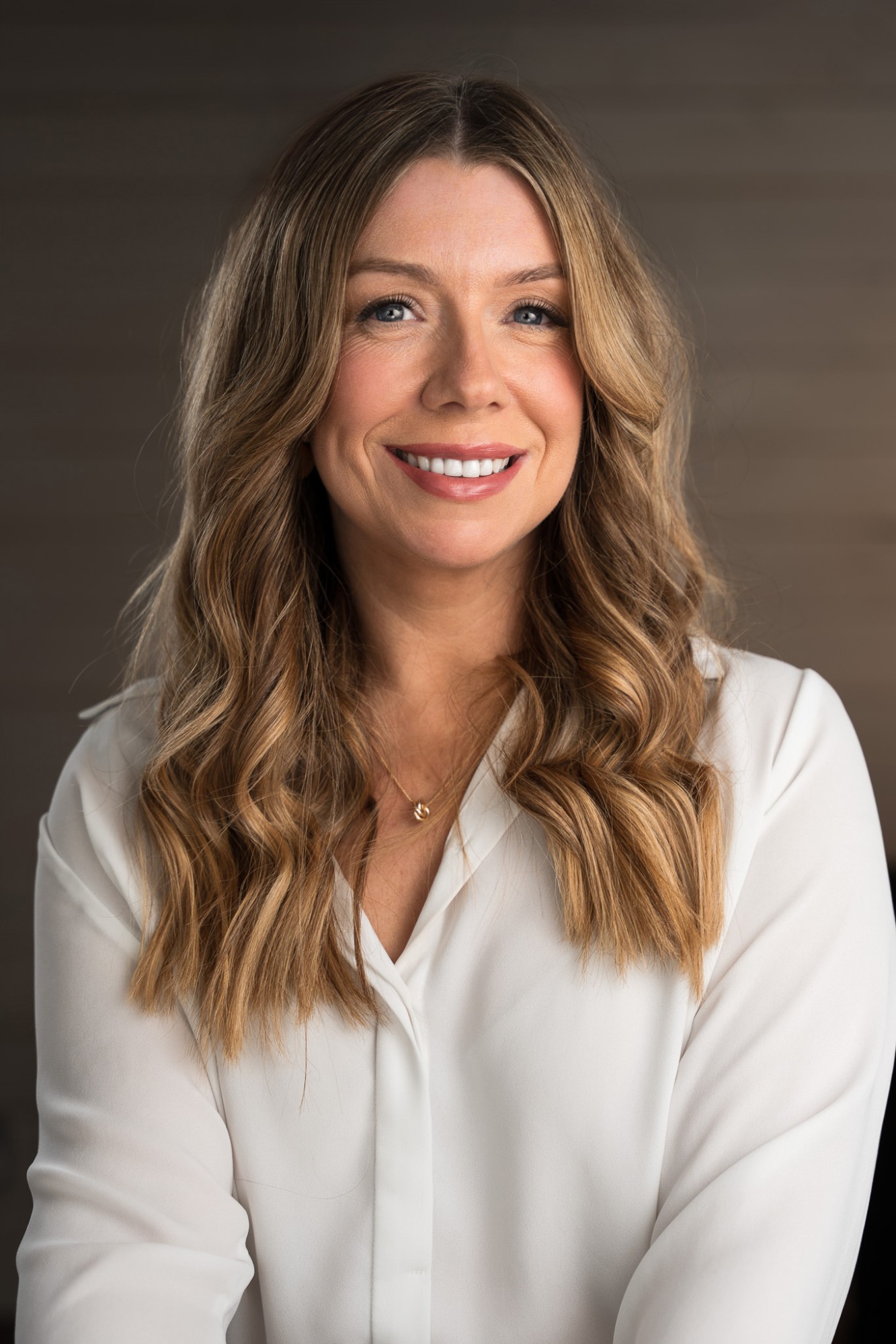 A smiling woman with long wavy hair in a white blouse