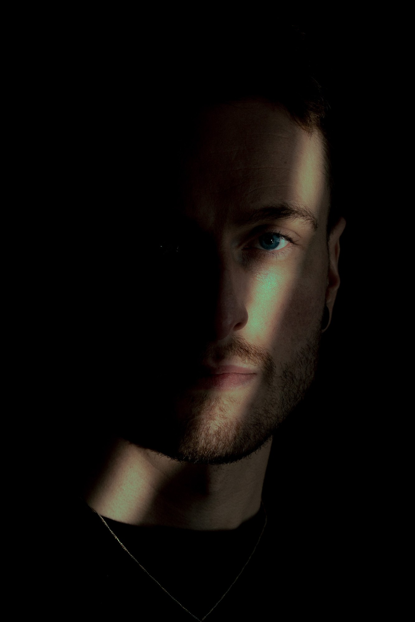 A bearded man, half his face lit by a shaft of light