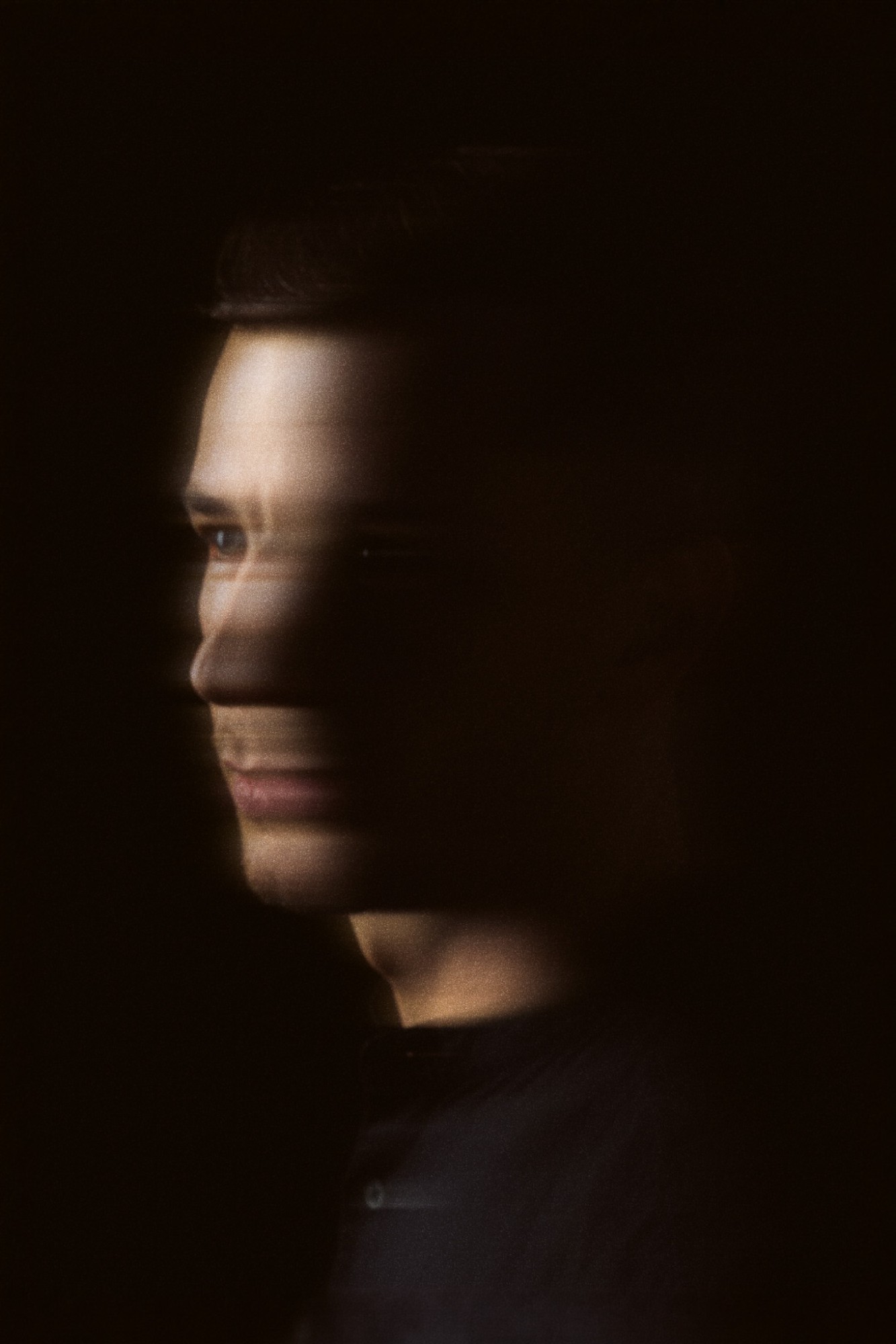 A man in profile, bands of warm light across his face in the dark