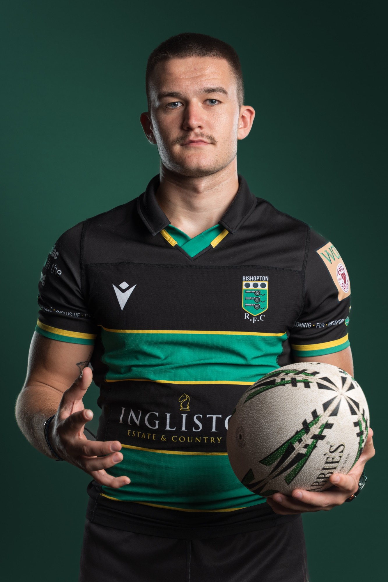 A Bishopton RFC player holding a rugby ball against a dark green backdrop