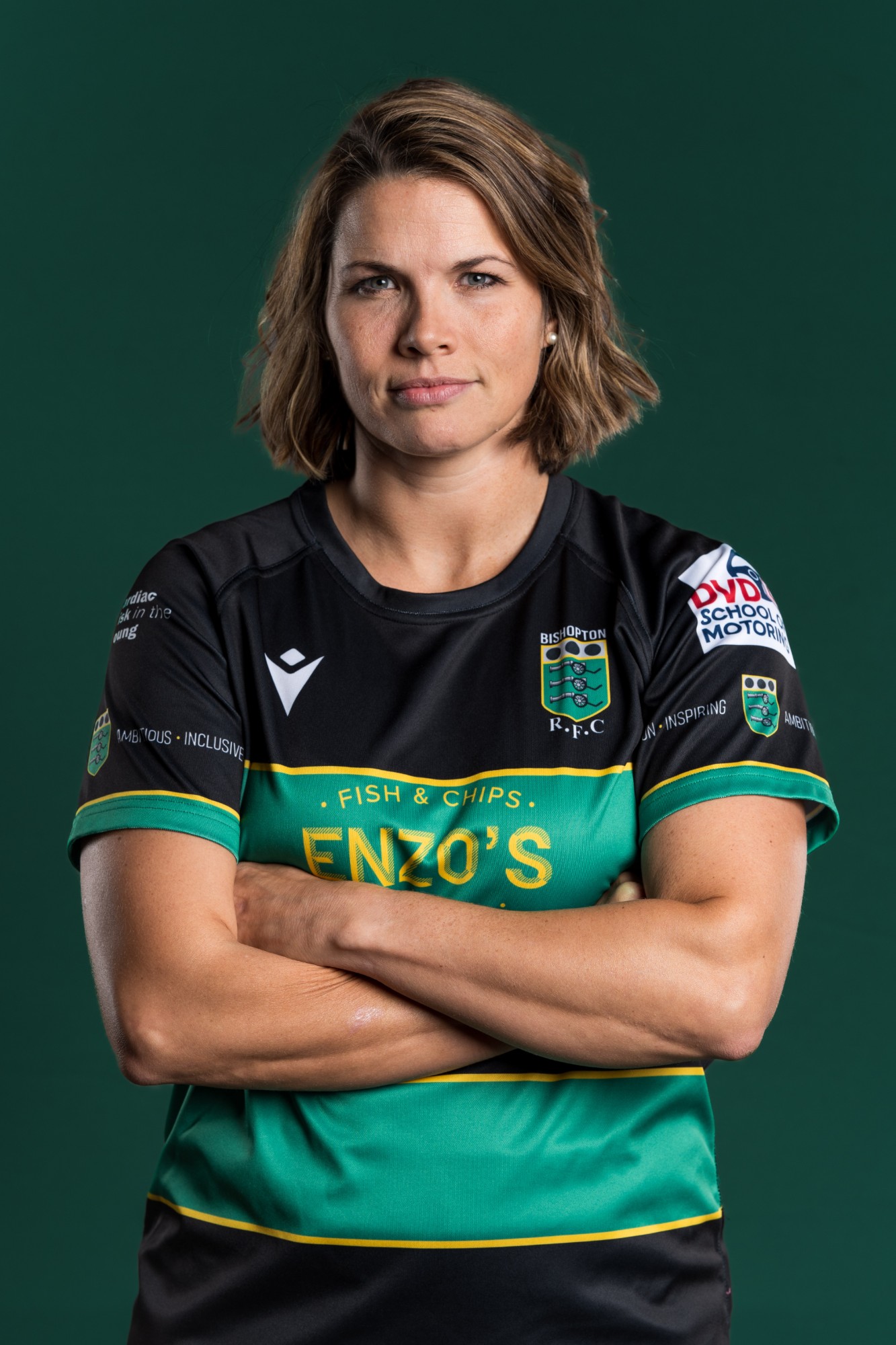 A Bishopton RFC player, arms folded, looking straight at the camera against a dark green backdrop