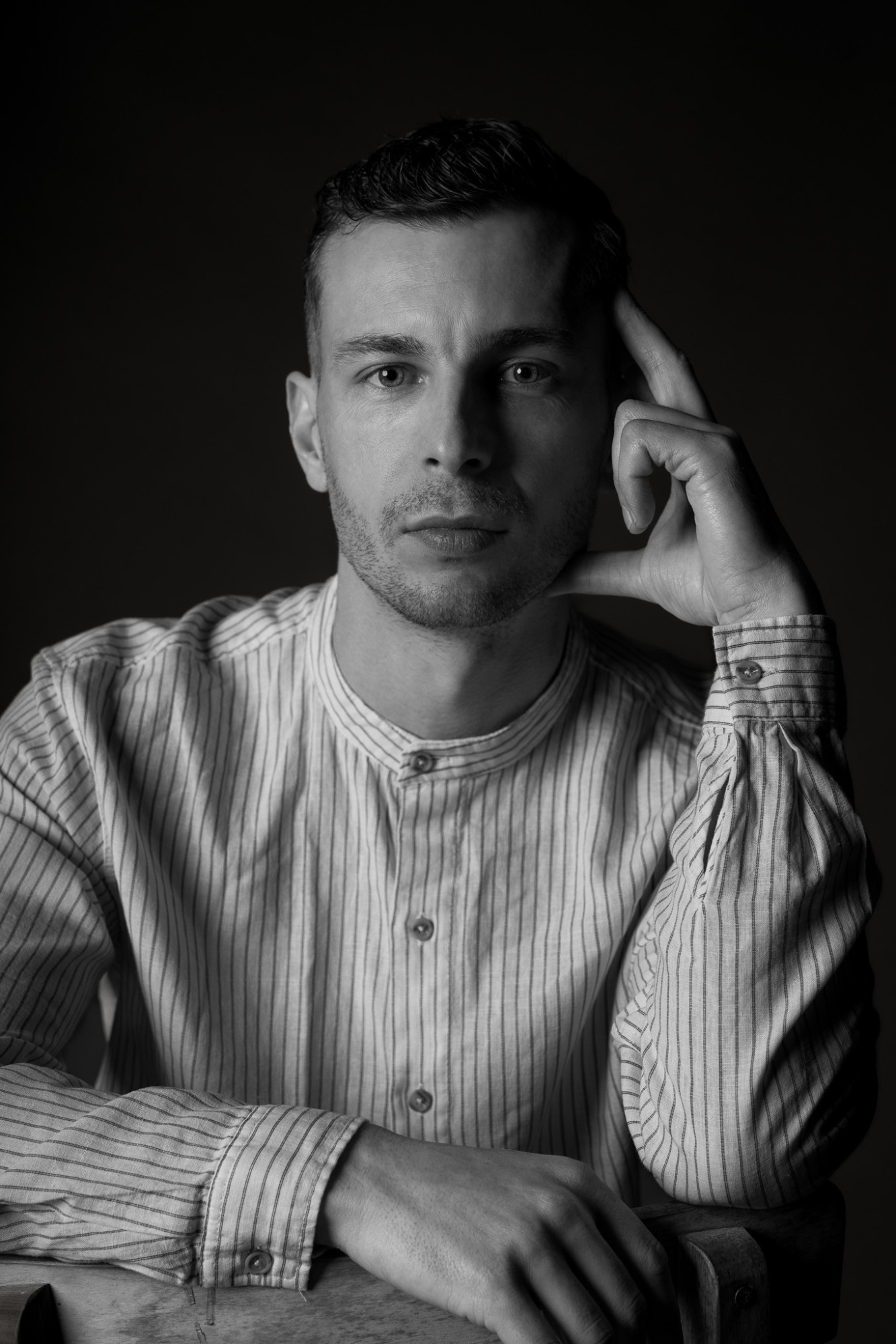 A man in a striped collarless shirt, head resting on his hand, in black and white
