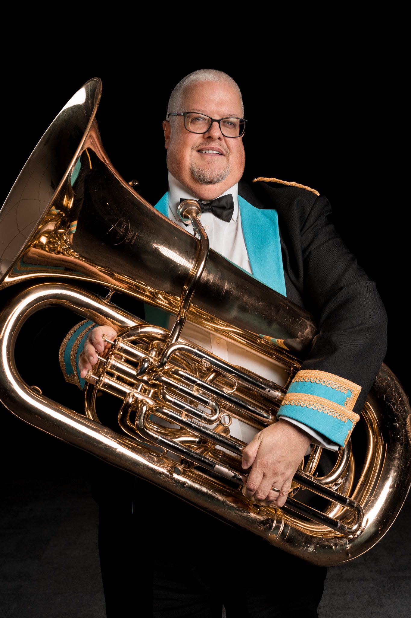 A brass band player holding a tuba against a black background